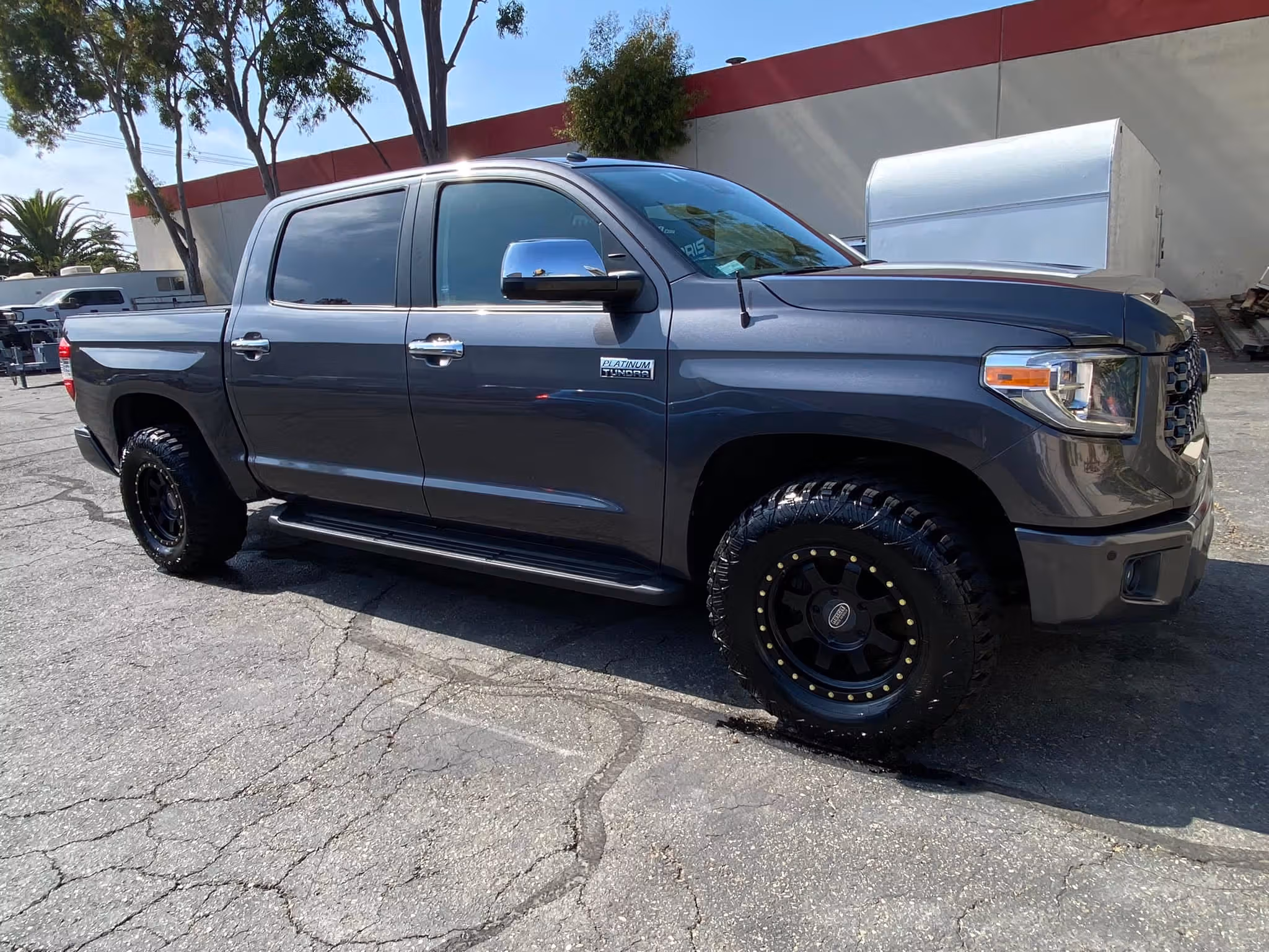 Gray Toyota Tundra Platinum pickup truck parked on cracked pavement under trees.