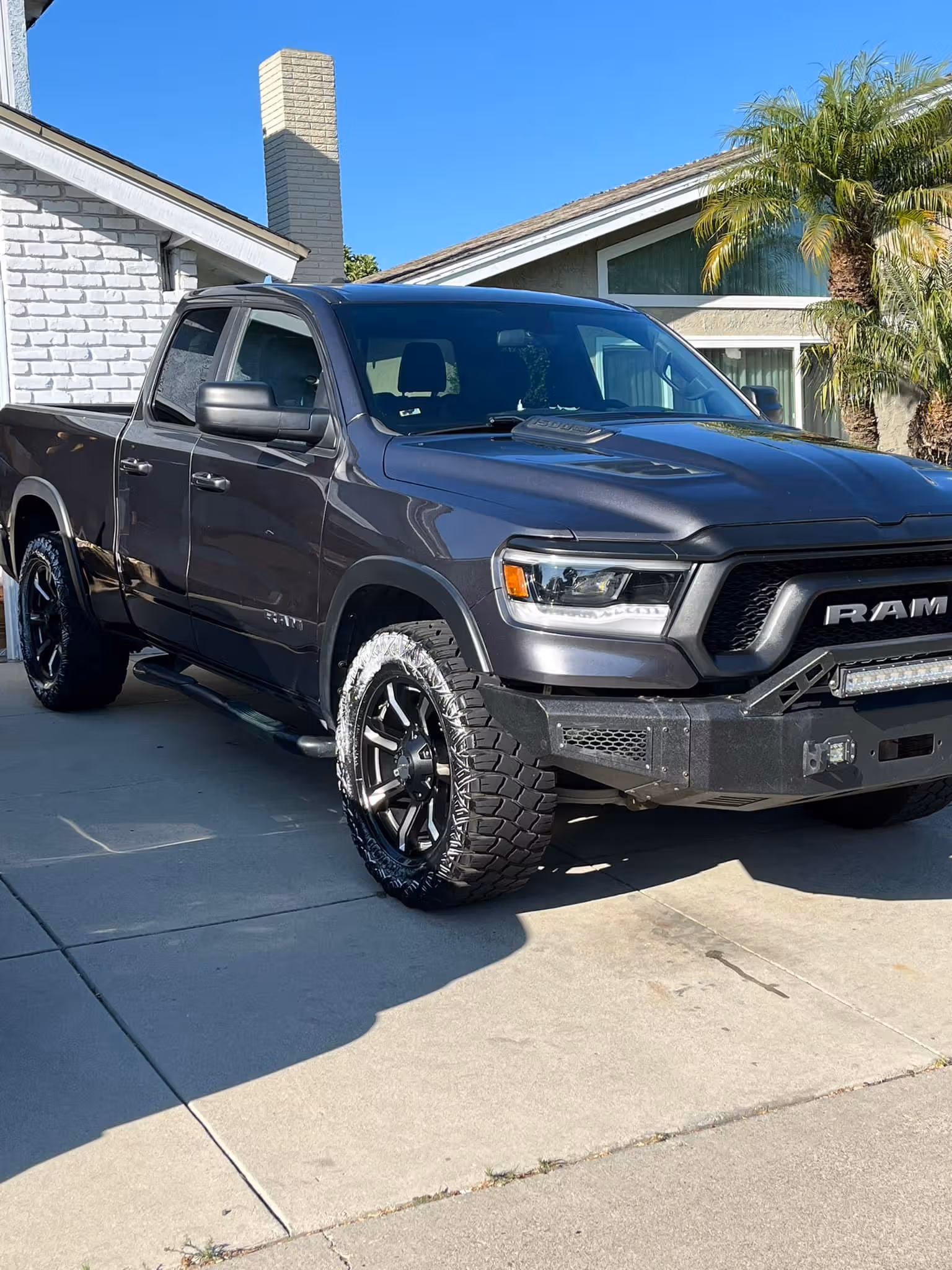 Black RAM pickup truck parked in driveway in front of house with palm trees and clear sky.