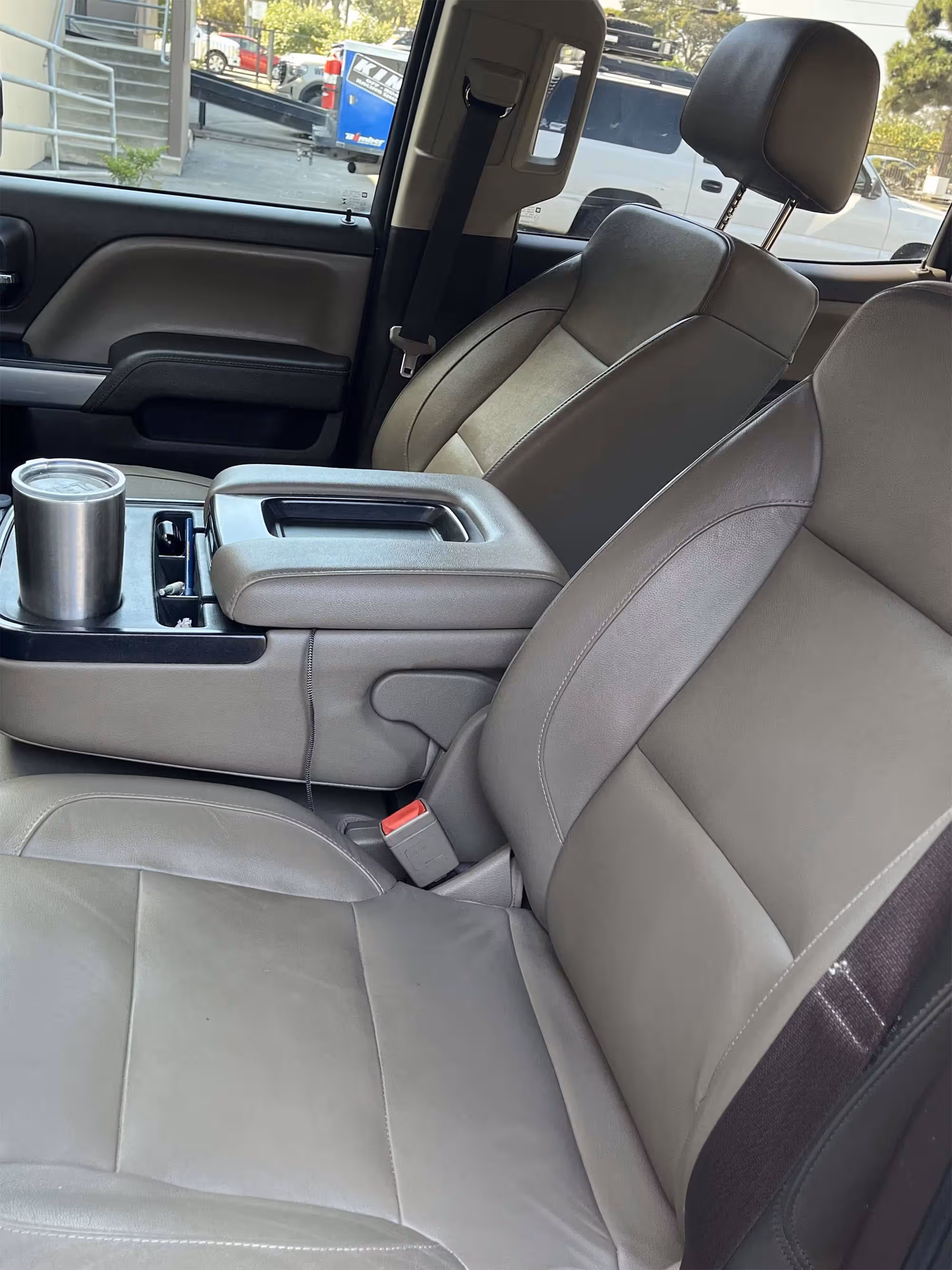 Close-up of a vehicle's front leather seats and center console with a stainless steel tumbler.